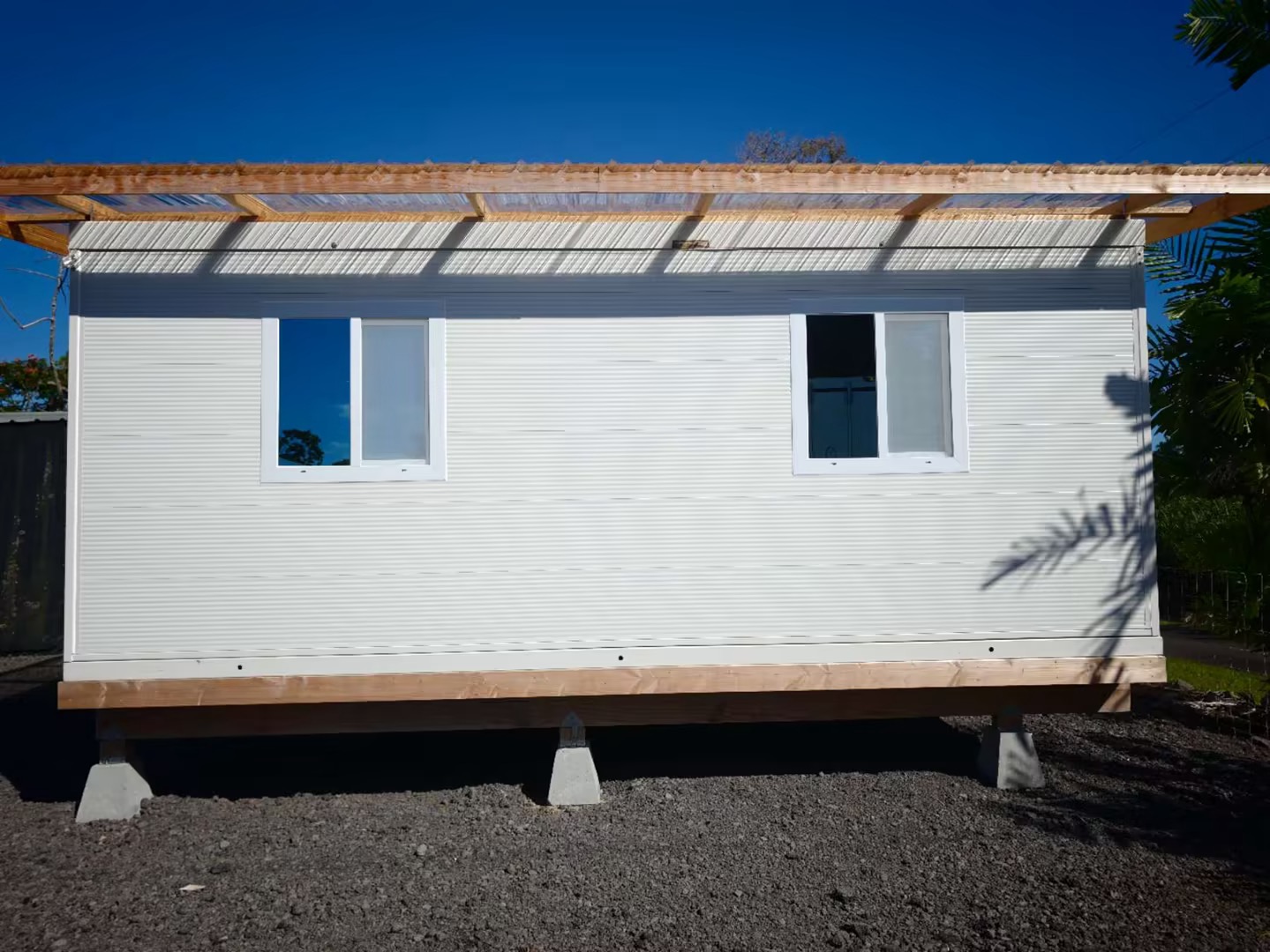 Installed container house with two side windows, raised timber base and an additional roof structure